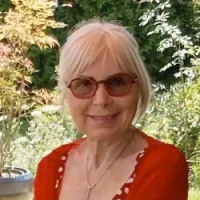 Portrait de Viviane Fontaine, habillée d'une jaquette rouge et posant devant les plantes de son jardin